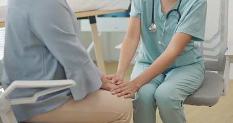 Obraz premium Close up Asian female doctor or nurse gently holds hands and talks with an elderly female patient in a clinic, providing comfort, empathy, and emotional care during a supportive medical consultation.