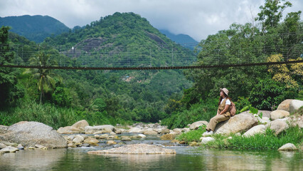 A woman sitting on the rock by the creek with forest and mountain views