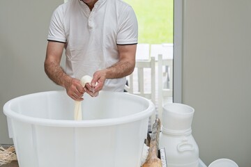 A skilled cheesemaker works on fresh cheese, stretching and shaping it in a white tub. This image represents traditional cheese-making, ideal for food blogs and artisanal product promotions.