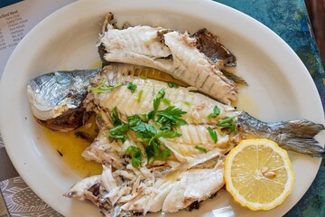 Enjoy this delicious grilled fish, seasoned with fresh parsley and served with a lemon slice. A healthy Mediterranean dish ideal for culinary projects, presented on a white plate.