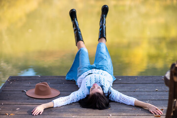 Autumn lake woman. She lies by a pond on a wooden pier in autumn and admires nature. The concept of tourism, weekends outside the city.