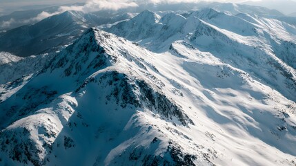 Aerial view captures extensive range of rugged, snow-covered mountain peaks under bright daylight.
