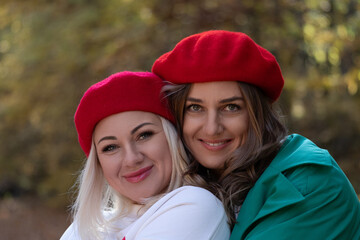 Berets Women Portrait: Outdoors autumn friendship photo shoot showcasing two smiling women wearing matching red berets.