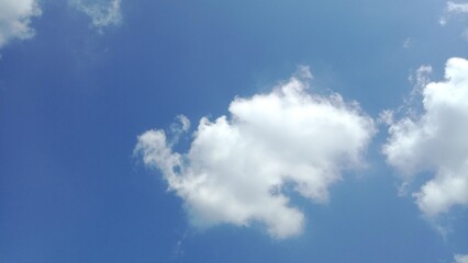 Bright blue summer sky with fluffy white cumulus clouds, perfect for background or weather themes.