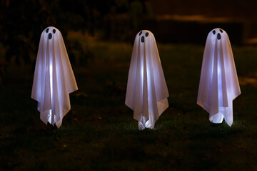 Three little white glowing ghosts in the yard, Halloween outdoor decoration for the festive holiday...
