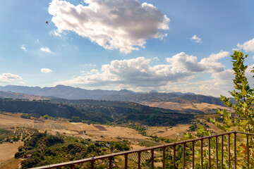 Expansive valley landscape in ronda, andalusia, spain, showing hills, cultivated fields, mountains, and a bird flying under a blue sky in ronda,malaga,spain