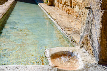 Fresh, clear water flowing from an old stone spout into a historic rustic trough, creating gentle ripples in ronda,malaga,spain