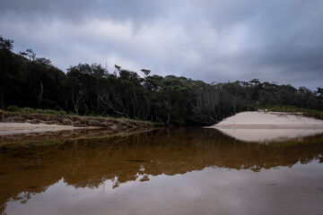 Reflective river at Kioloa beach with trees and cloudy sky