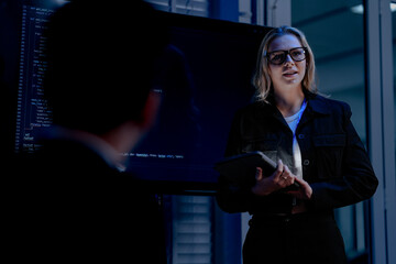 A confident female tech leader presents complex information on a large screen using a tablet and stylus leading a training session for her diverse team in a modern office hub.