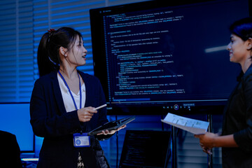 A diverse team with an Asian female, an Indian female and a Caucasian male collaborates in a high-tech office. They are standing and discussing a project.