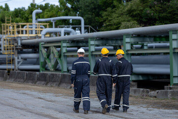 Three industrial engineer walking together along pipeline facility, wearing safety gear, symbolizing inspection, teamwork and daily operations in oil, gas or energy related infrastructure.
