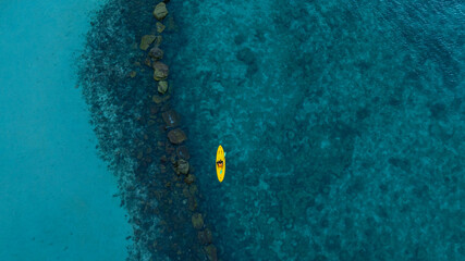 aerial view  woman bright yellow kayak with  in the vast expanse of crystal clear turquoise water. The seabeds rocky texture is visible beneath the surface, concept marine environment.