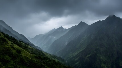 Dramatic mountain range descends into a misty, shadowed valley under heavy cloud cover