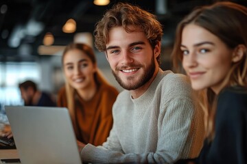 Smiling young man and two women working together at a laptop in a modern office environment with warm lighting