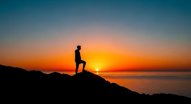 Silhouette of a man standing on a hill at sunset, looking out over the ocean with vibrant orange and blue sky, enjoying the view
