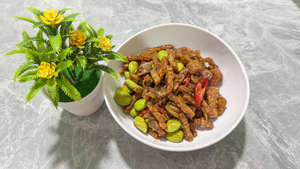 Stir Fried Tempeh with Petai Beans and Chili on White Bowl, Traditional Indonesian Food with Spicy Sweet Soy Sauce on Marble Table Background