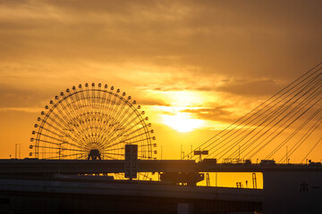夕陽に染まる観覧車と橋を渡る車のシルエット