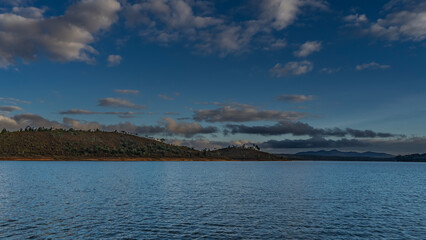 Beautiful lake landscape. The evening golden hour. Ripples on calm blue water. There is green vegetation on the hilly shores. Picturesque clouds in the sky. Madagascar. Lake Mantasoa