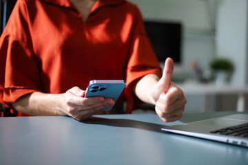 Person giving thumbs up while using smartphone. Symbol of success, approval, positive communication, and modern digital lifestyle.