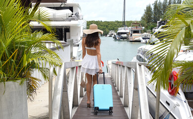 Young woman with small blue luggage walks near the boat marina