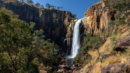Tall cascade plunges down rugged cliff face into natural pool surrounded by scrubland vegetation