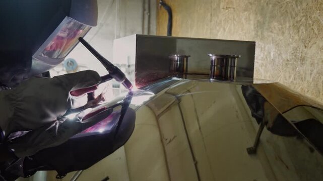An industrious and technical mood is captured by a close-up of a welder in protective gear using a welding torch, with the bright arc and reflection visible in the shield and surrounding surfaces
