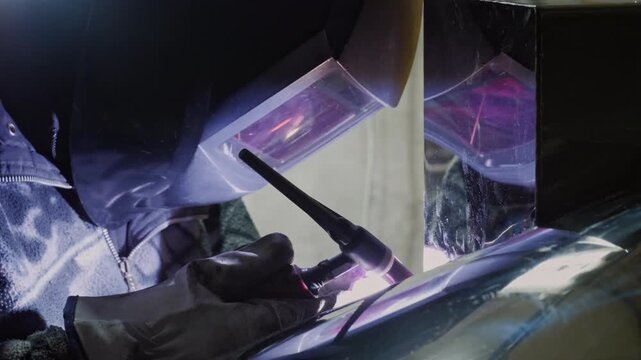 An industrious and technical mood is captured by a close-up of a welder in protective gear using a welding torch, with the bright arc and reflection visible in the shield and surrounding surfaces