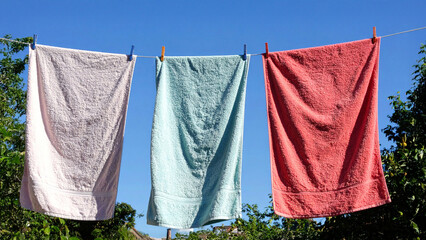 Soft colorful towels and fresh laundry hanging on clothesline swaying gently under radiant sunlight with blue sky and garden symbolizing harmony, hope, and renewal