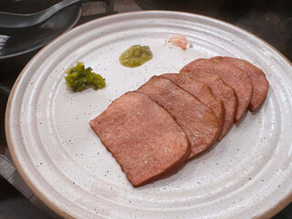 close-up of several slices of cooked, thinly sliced Chinese ham served on a rustic speckled ceramic plate