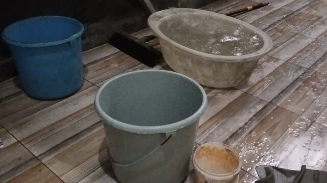 Various buckets and cleaning tools were placed on the wet ceramic floor, to collect rainwater from the leaking roof tiles.