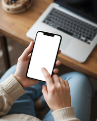 Casual tech moment at home person using smartphone with blank screen, seated near laptop on wooden table. Cozy, modern setup for remote work or digital lifestyle