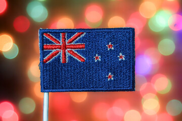 New Zealand national flag (Union Jack & Southern Cross) against colorful festive bokeh lights. Symbolizes Oceania, sports, travel, national day, Christmas, and New Year celebration themes.