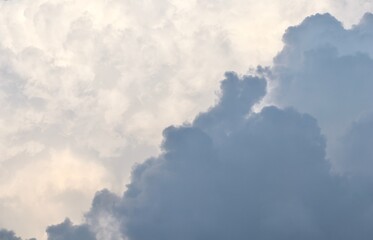 A dramatic diagonal contrast between a heavy, dark grey storm cloud and a bright, ethereal mass of sunlit white clouds, creating an abstract and moody sky background.