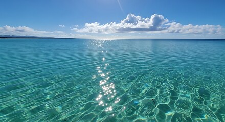 A vast, calm turquoise sea glittering under a bright sun, with a clear blue sky and a hazy coastline.