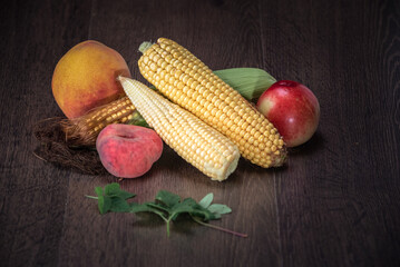 Fresh assortment of colorful fruits and vegetables including peaches, corn, and apples arranged beautifully on a rustic wooden surface showcasing natural textures and vibrant colors