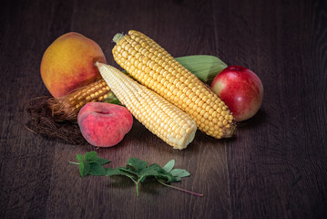 Fresh assortment of colorful fruits and vegetables including peaches, corn, and apples arranged...