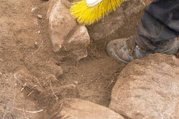 An archaeologist's boot and brush cleaning an excavation site The Careful Process of Discovery