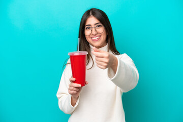 Young caucasian woman drinking soda isolated on blue background making money gesture