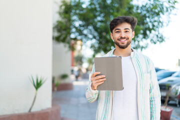 Handsome Arab man holding a tablet at outdoors smiling a lot