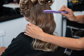 Fototapeta premium Stylist combing wavy hair in a salon, preparing for an elegant hairstyle in a modern beauty studio during a weekday
