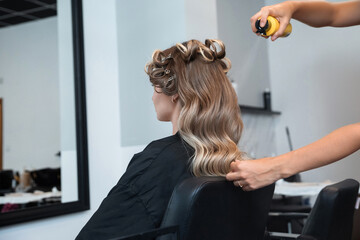 Stylist applies hair spray to create curls during a hair styling session at a salon in the afternoon