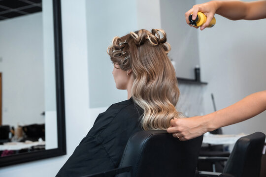 Stylist applies hair spray to create curls during a hair styling session at a salon in the afternoon