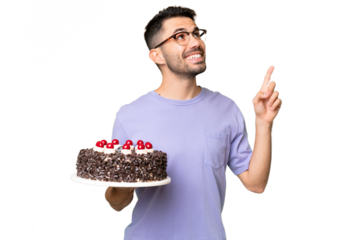 Young caucasian man holding birthday cake isolated on green chrome background pointing up a great idea