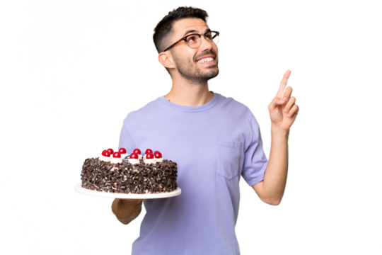 Young caucasian man holding birthday cake isolated on green chrome background pointing up a great idea