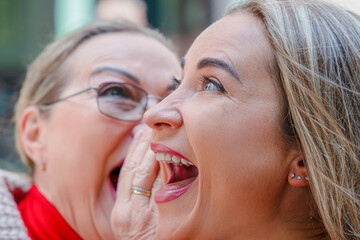 Two women share a joyful moment in a lively outdoor setting while enjoying a lighthearted conversation