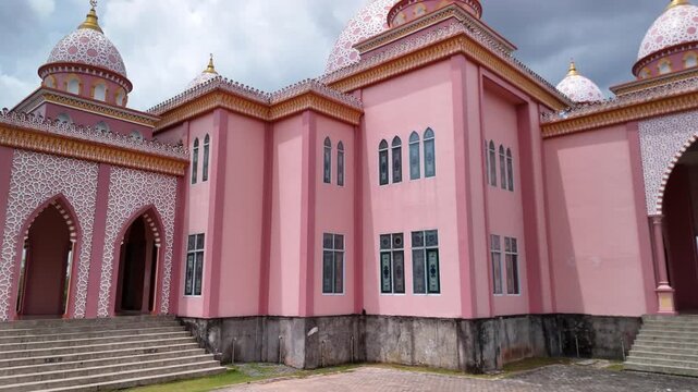 Aerial view of the pink AnNur Mosque in Bintan showcasing its elegant domes and reflection surrounded by lush greenery and tranquil water scenery