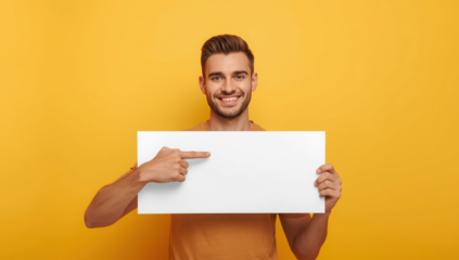 Transparent smiling man pointing at a blank white sign board he is holding against a yellow wall, copy space mockup