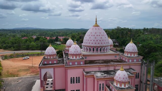 Aerial view of the pink AnNur Mosque in Bintan showcasing its elegant domes and reflection surrounded by lush greenery and tranquil water scenery