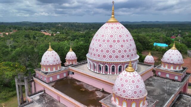 Aerial view of the pink AnNur Mosque in Bintan showcasing its elegant domes and reflection surrounded by lush greenery and tranquil water scenery