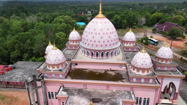 Aerial view of the pink AnNur Mosque in Bintan showcasing its elegant domes and reflection surrounded by lush greenery and tranquil water scenery